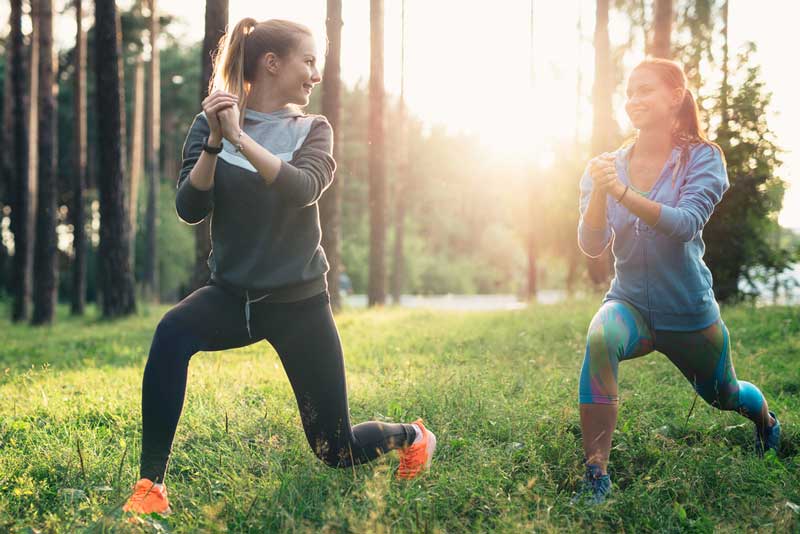 Two athletic female friends wearing jumpsuits doing lunges together training outdoors.