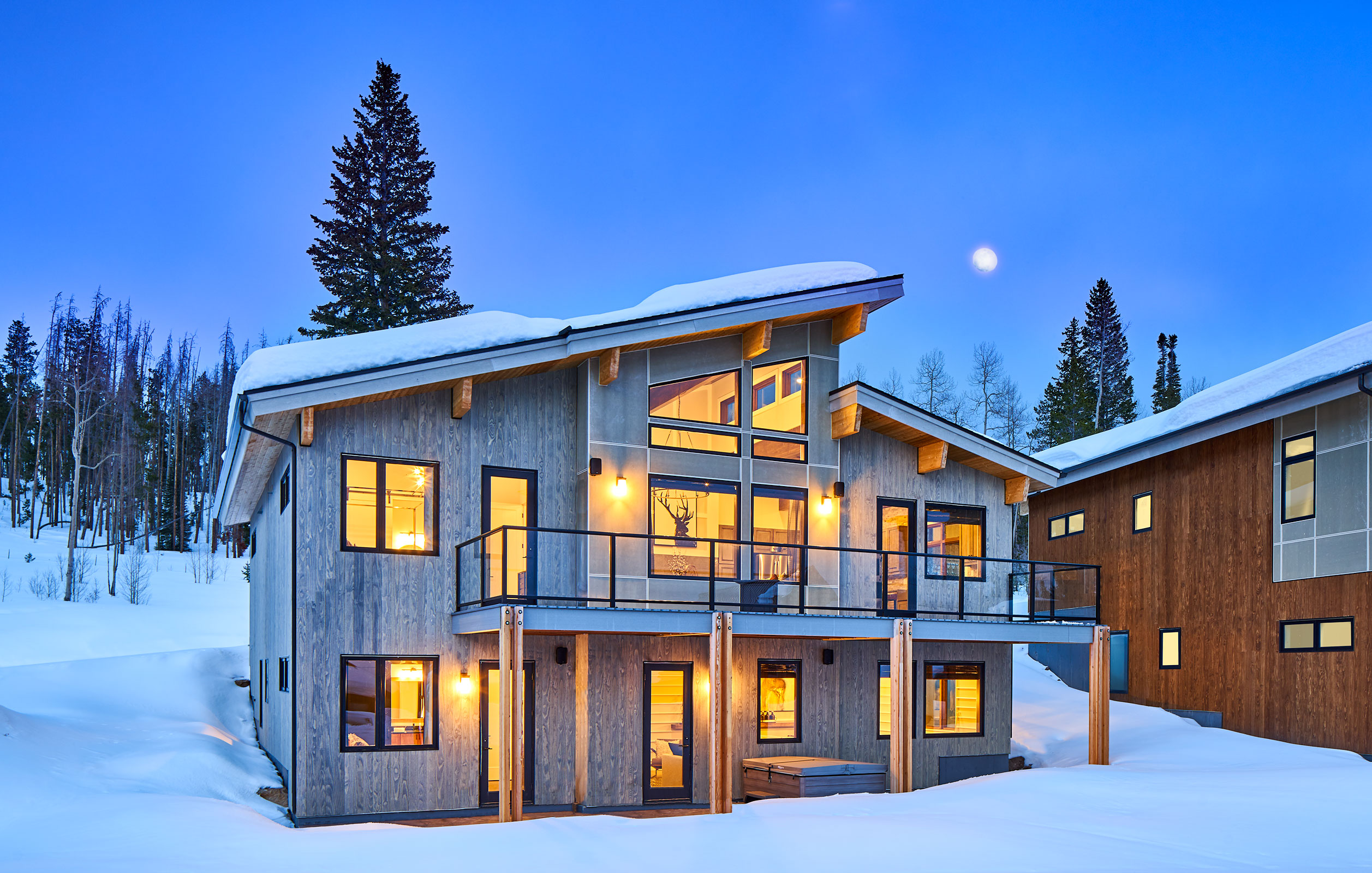 Mountain cabin home at dusk with lights on, covered in snow